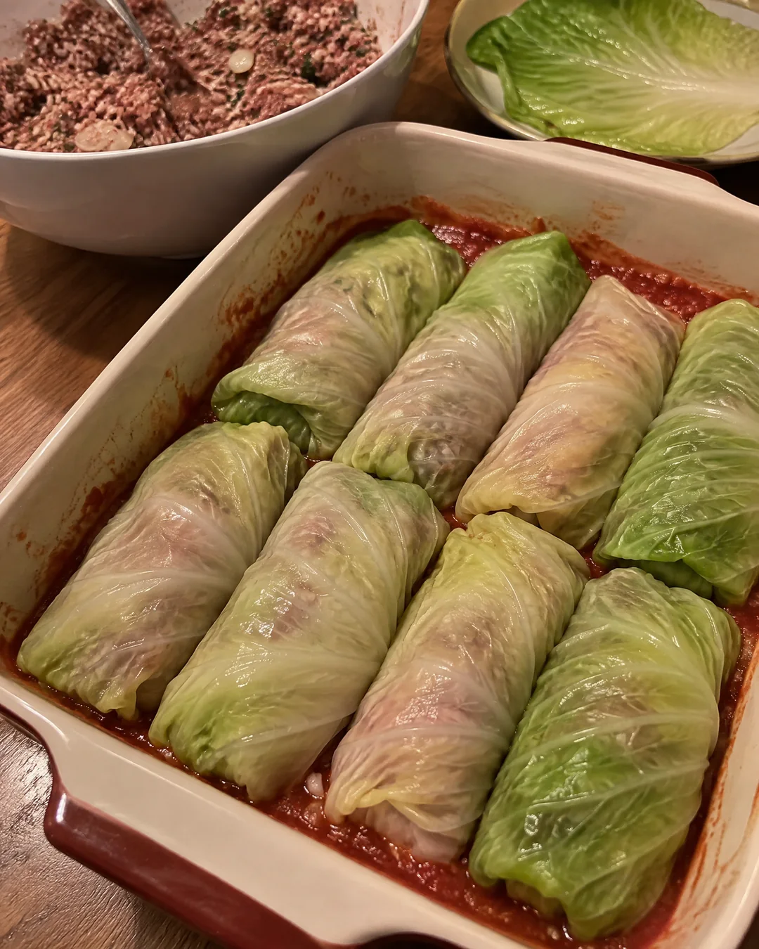 Raw stuffed cabbage rolls packed seam side down in a baking dish over tomato sauce