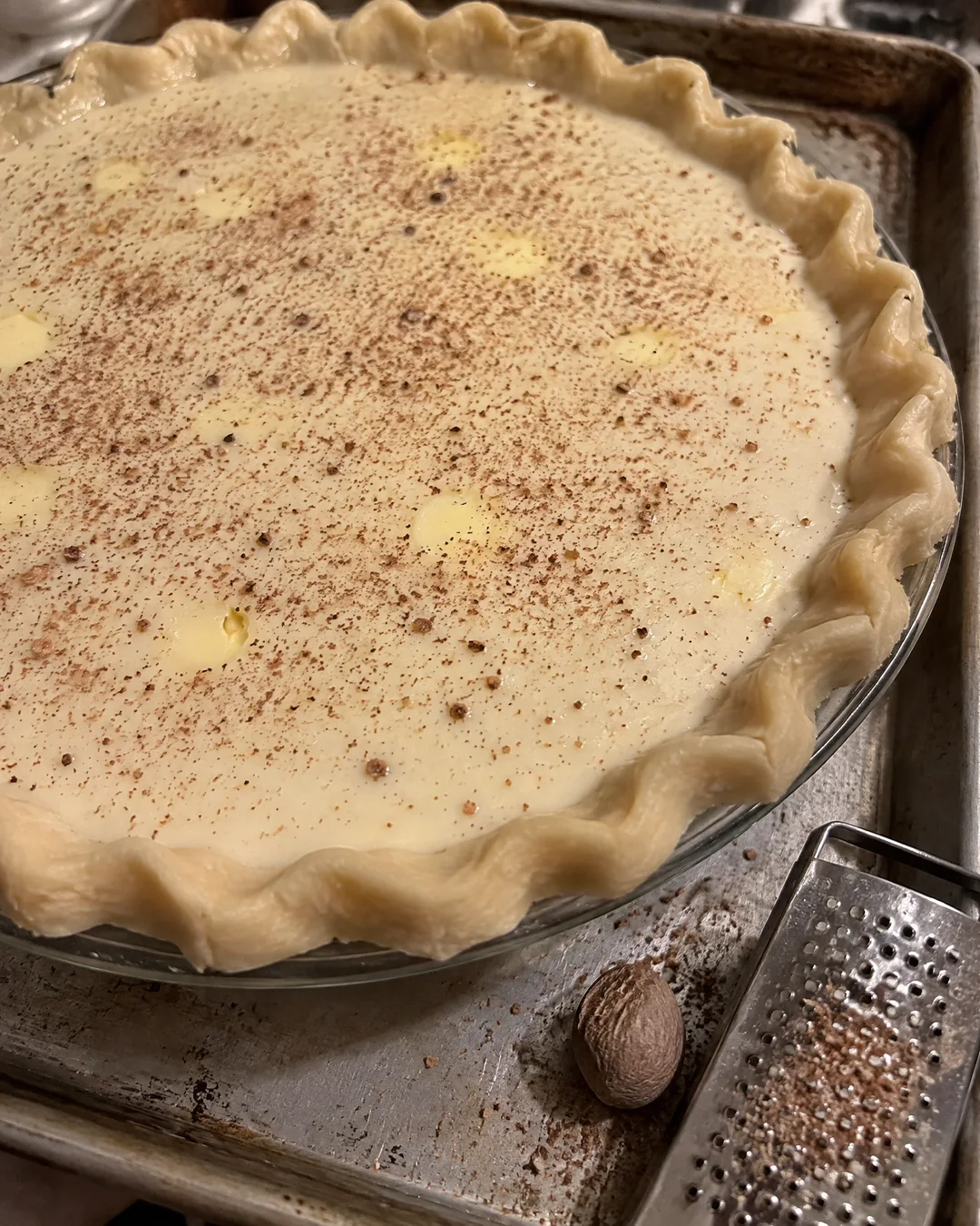 An unbaked sugar cream pie, the crust filled with cream, dotted with butter and dusted with nutmeg before going into the oven