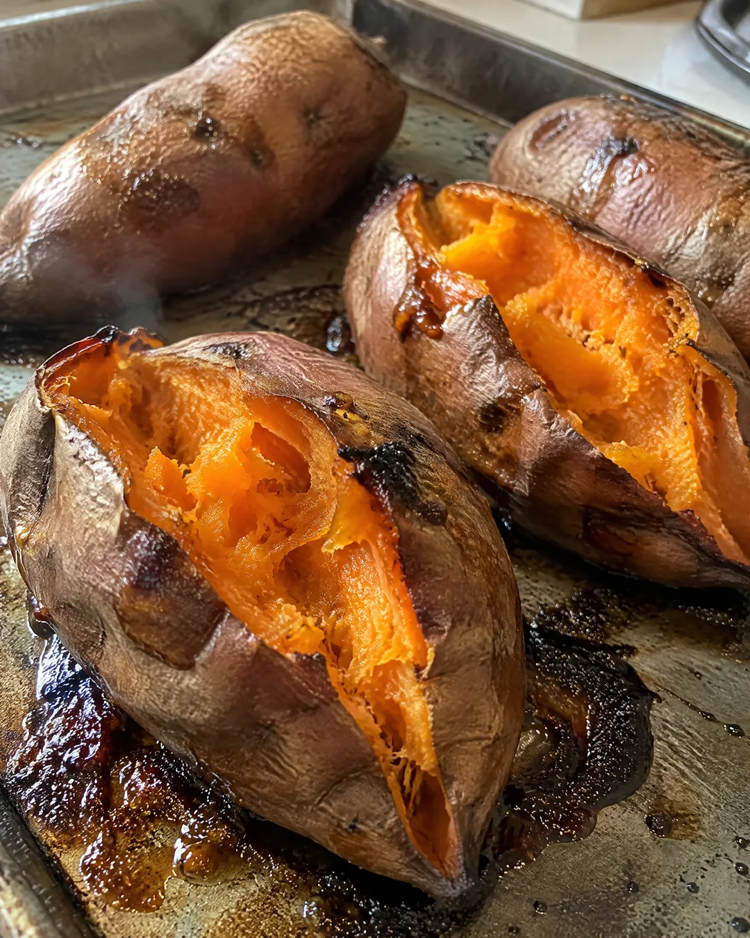 Baked sweet potatoes split open with the sugar bubbling out