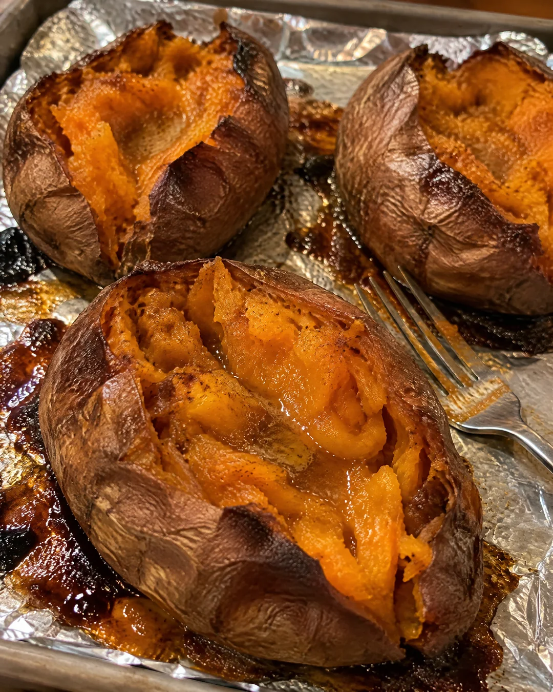 Baked sweet potatoes split open on a baking sheet with caramelized syrup for sweet potato pound cake