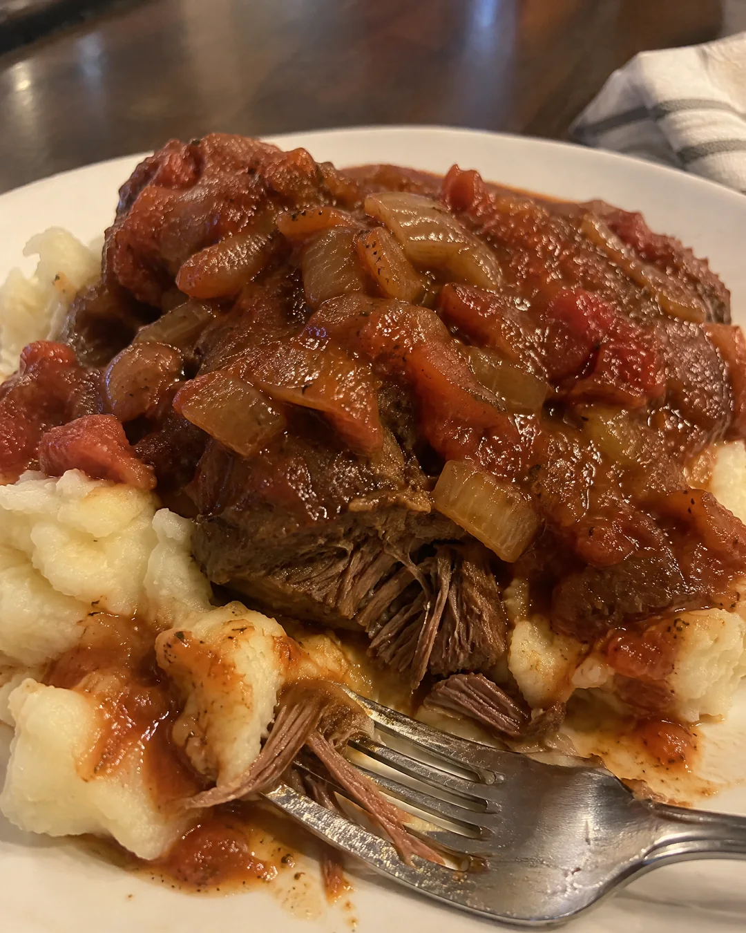 Swiss steak served over mashed potatoes with the chunky tomato and onion gravy running down the sides