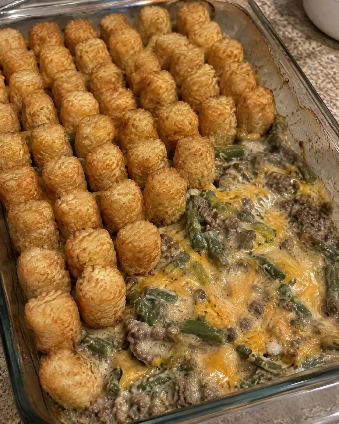 Frozen tater tots being arranged standing on end in rows over the beef mixture