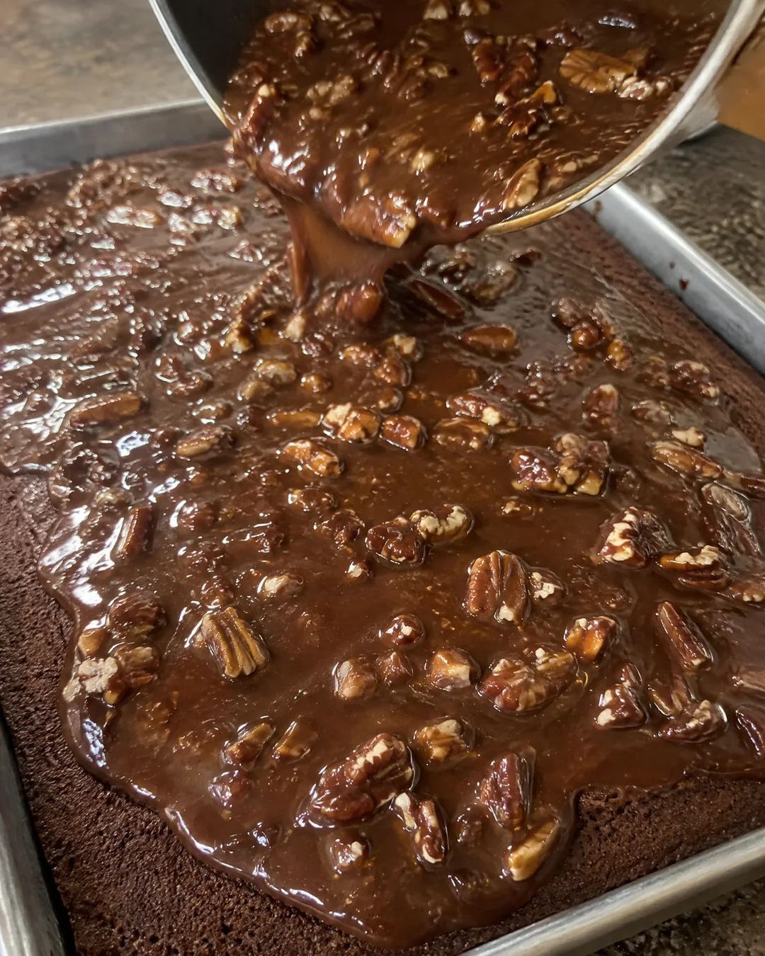 Pouring the warm chocolate pecan frosting over the hot sheet cake