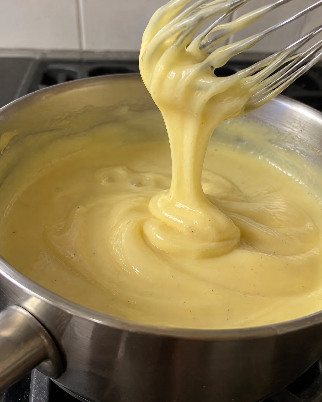 Thick vanilla custard falling from a whisk in heavy ribbons