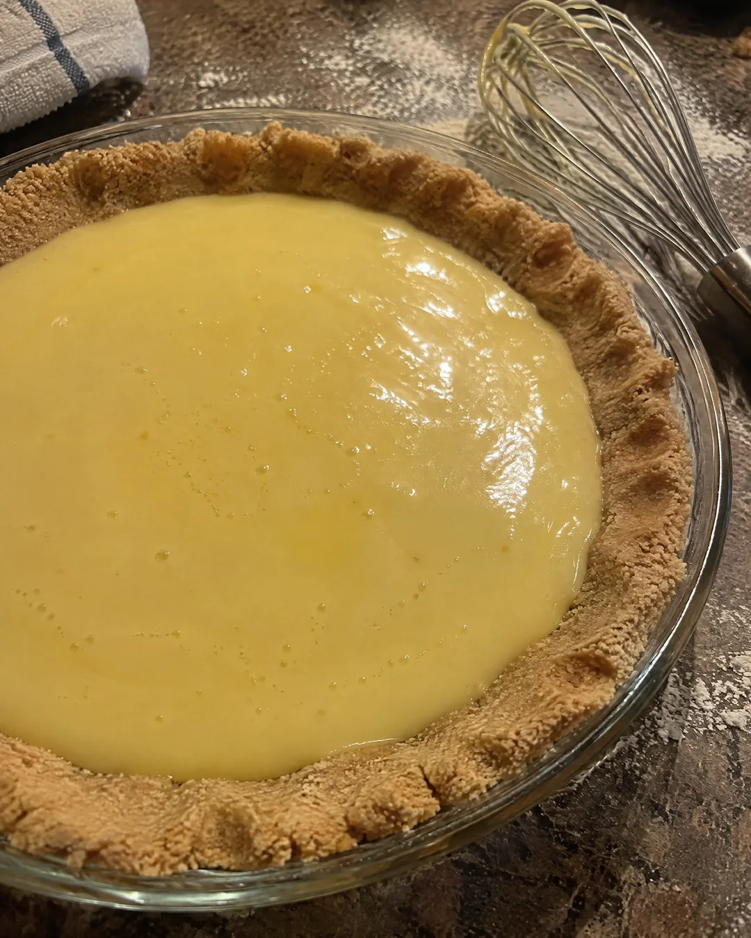 A lazy press-in pie crust pressed by hand into a pie plate with pale custard filling being poured into it