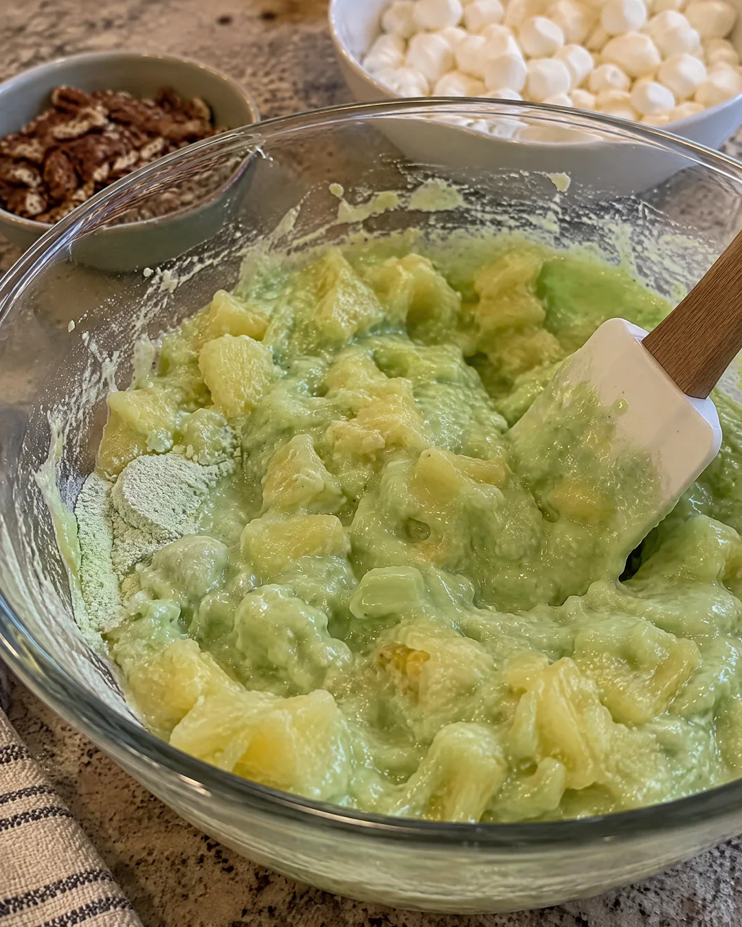 Dry pistachio pudding mix being stirred into crushed pineapple in a glass bowl