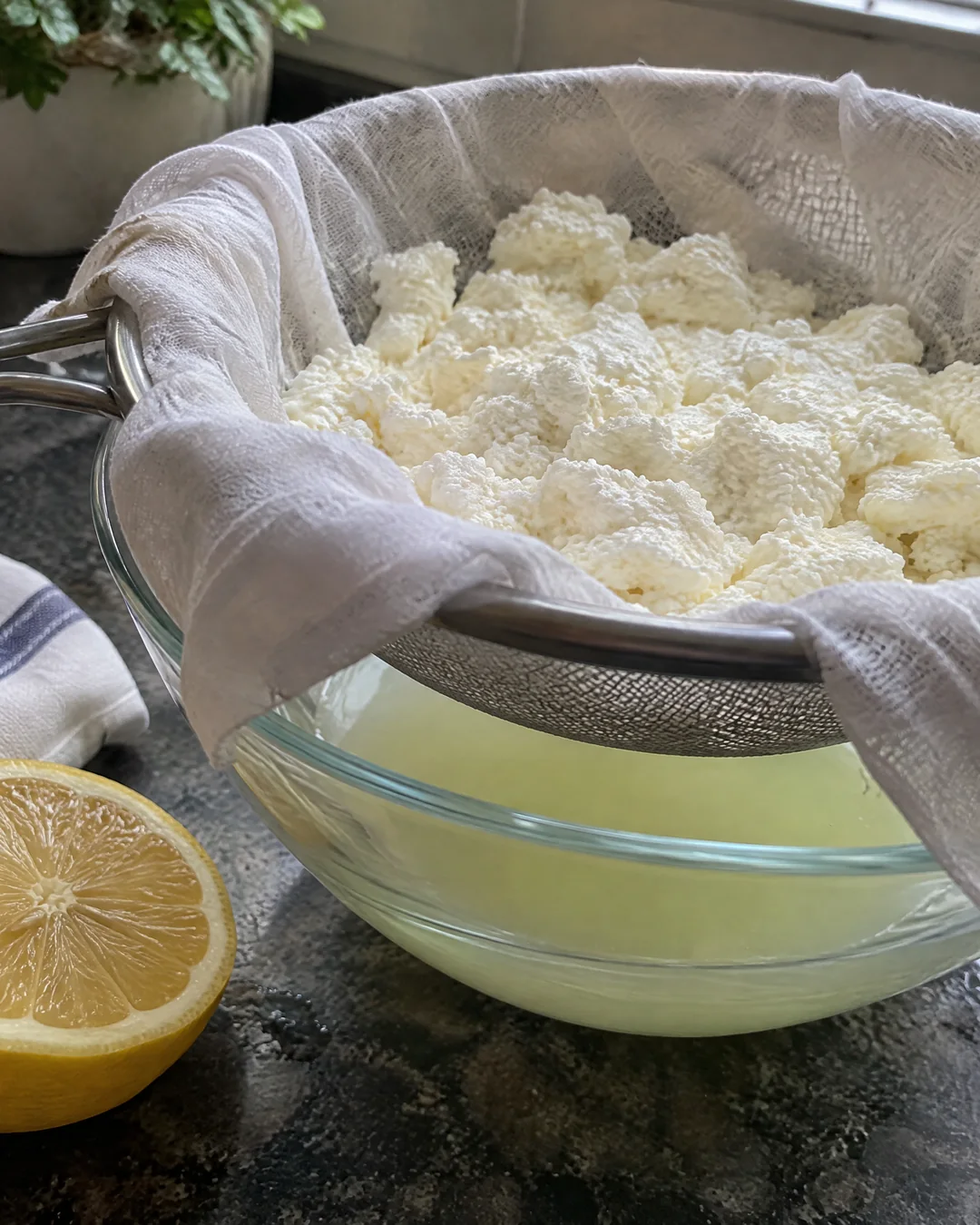 Fresh homemade curds draining in a towel-lined sieve over a bowl